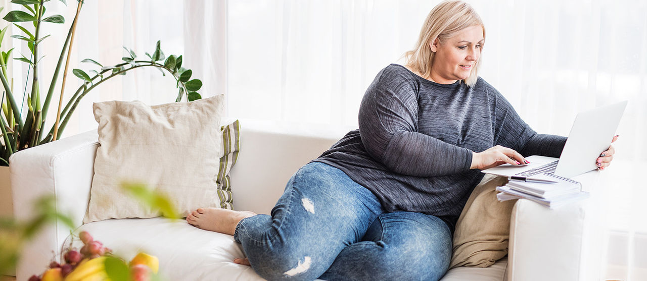 A woman reads on a laptop computer while sitting on her couch.